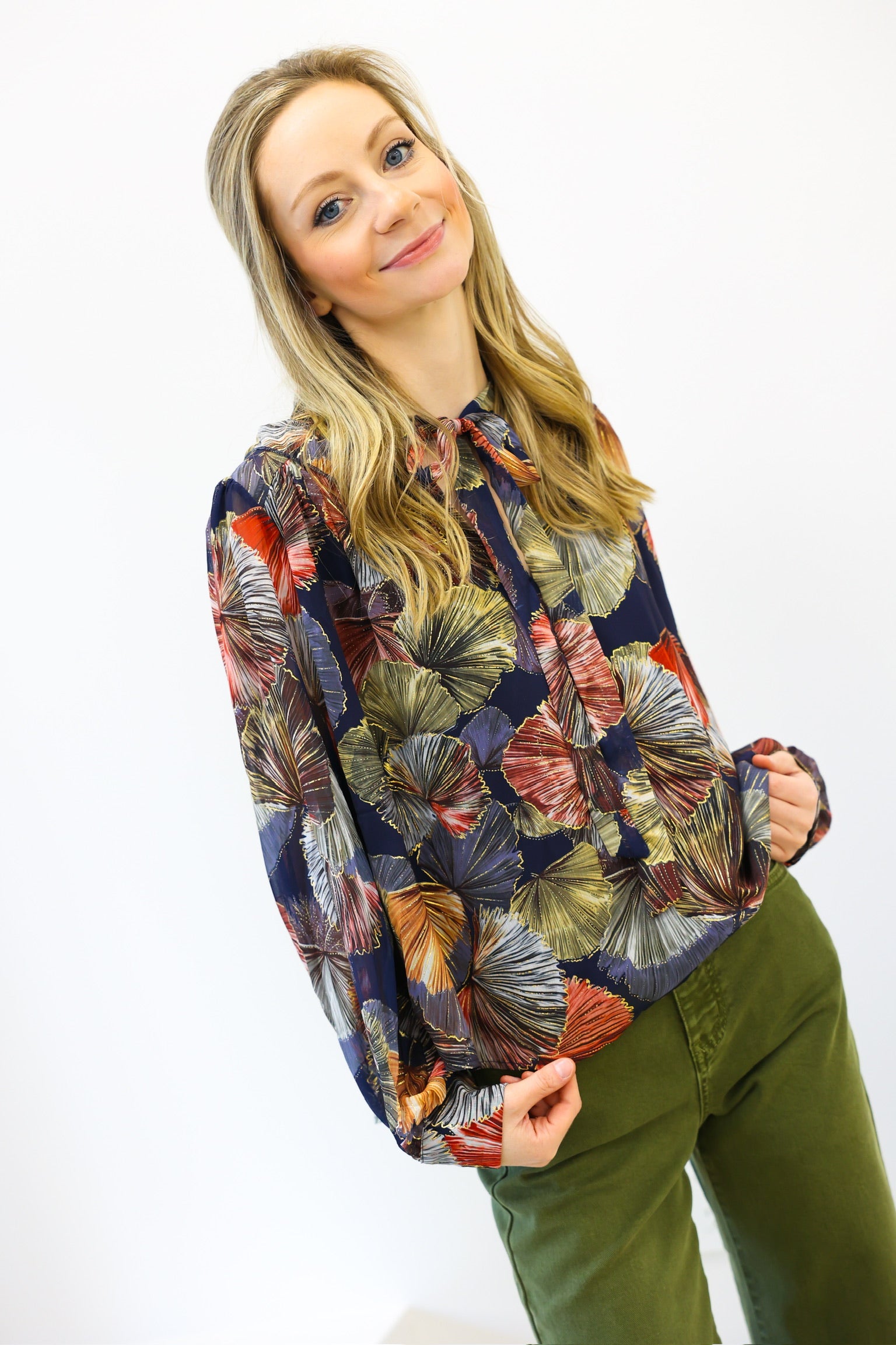 Woman wearing a colorful patterned shirt and green pants on a white background