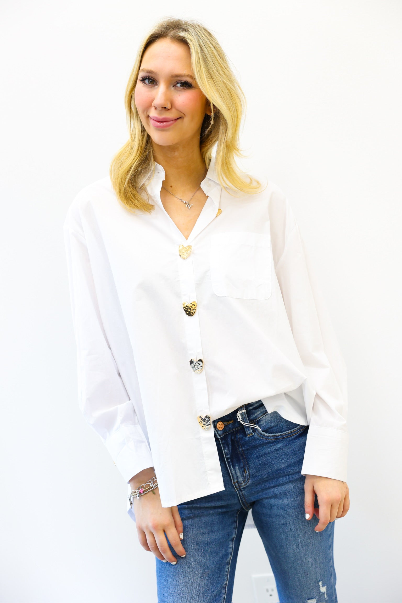 Woman wearing a white blouse with gold buttons and blue jeans on a white background