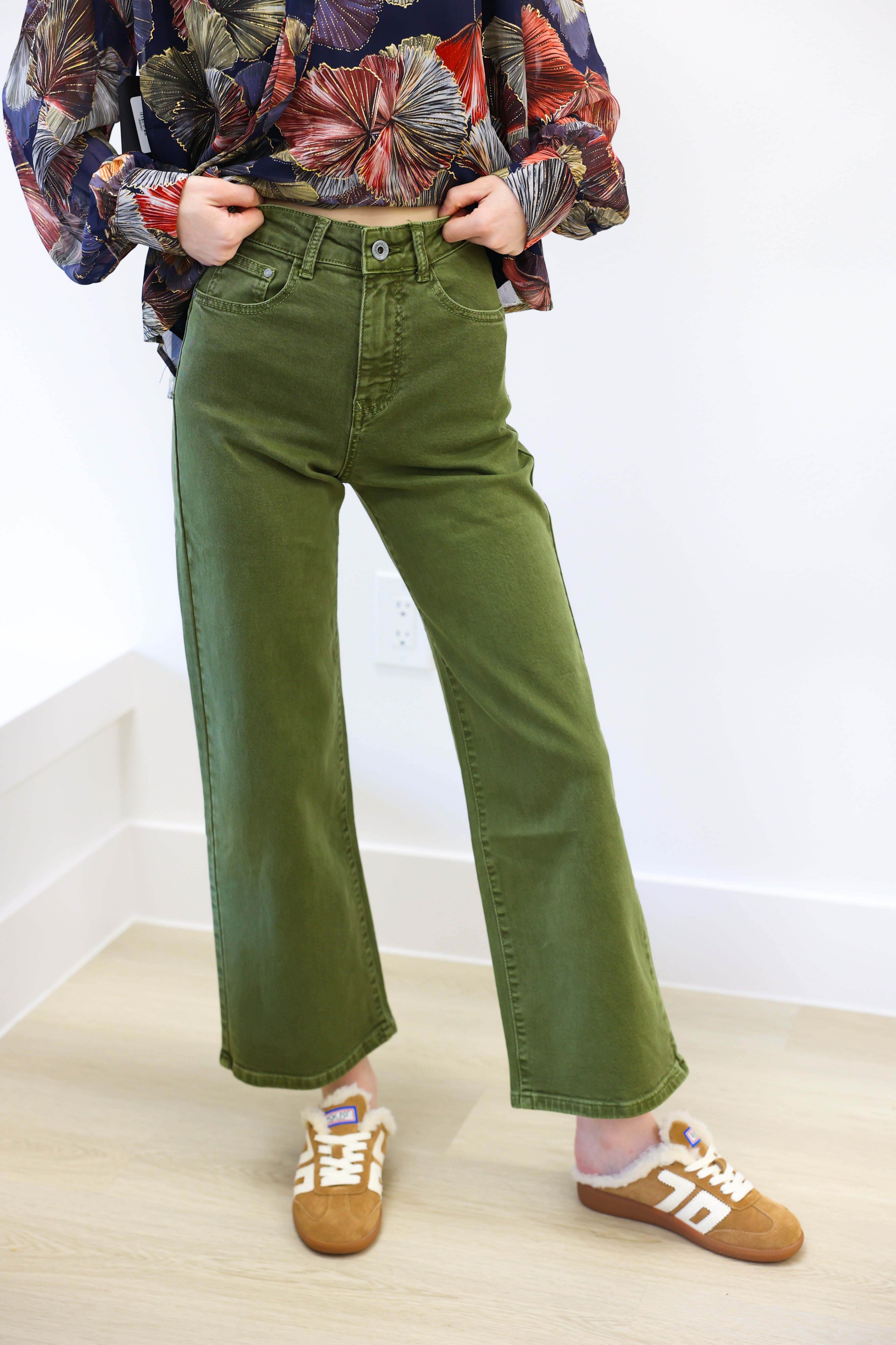 Person wearing green wide-leg jeans and a colorful patterned shirt on a white background