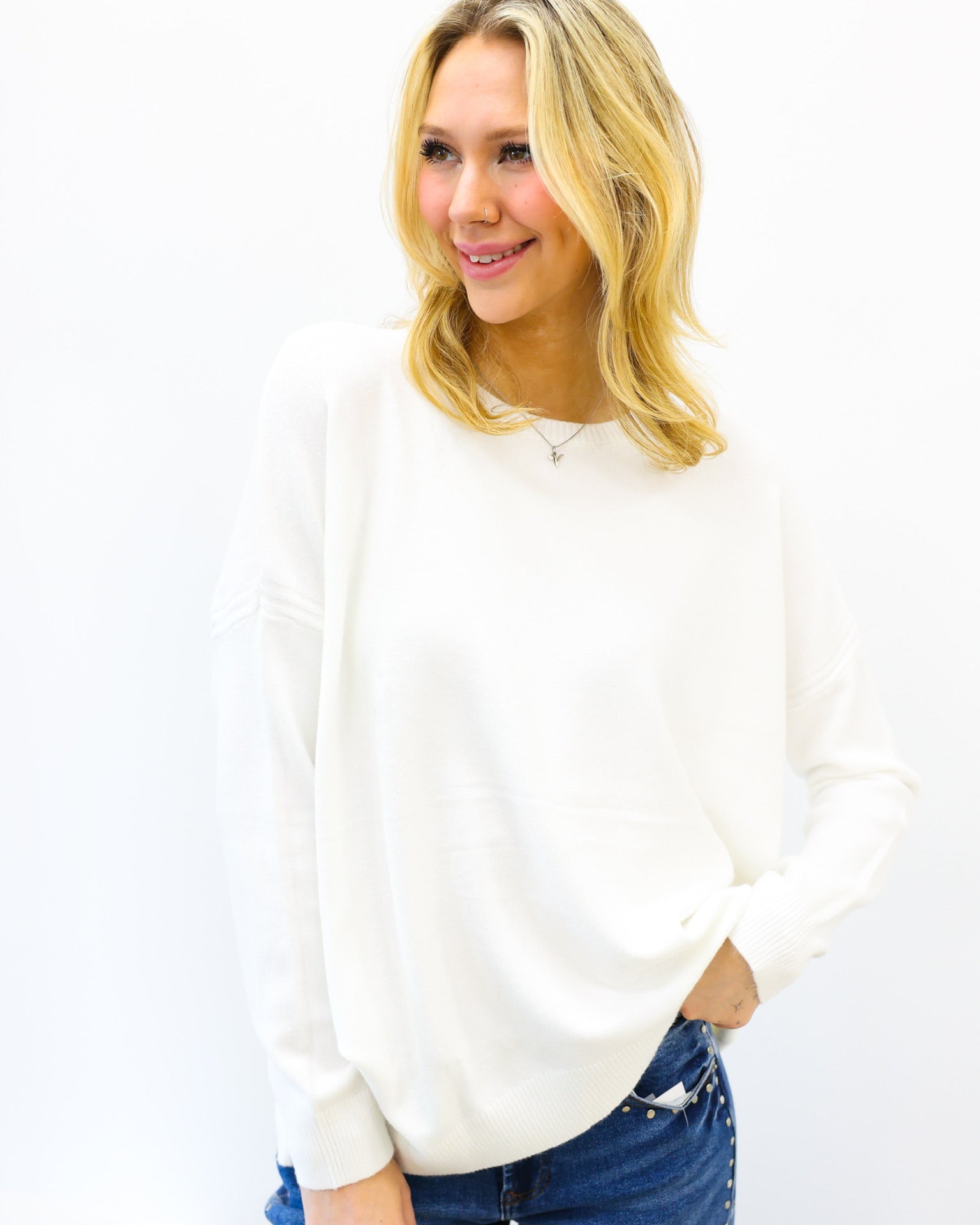 Woman wearing a white sweater and blue jeans against a white background
