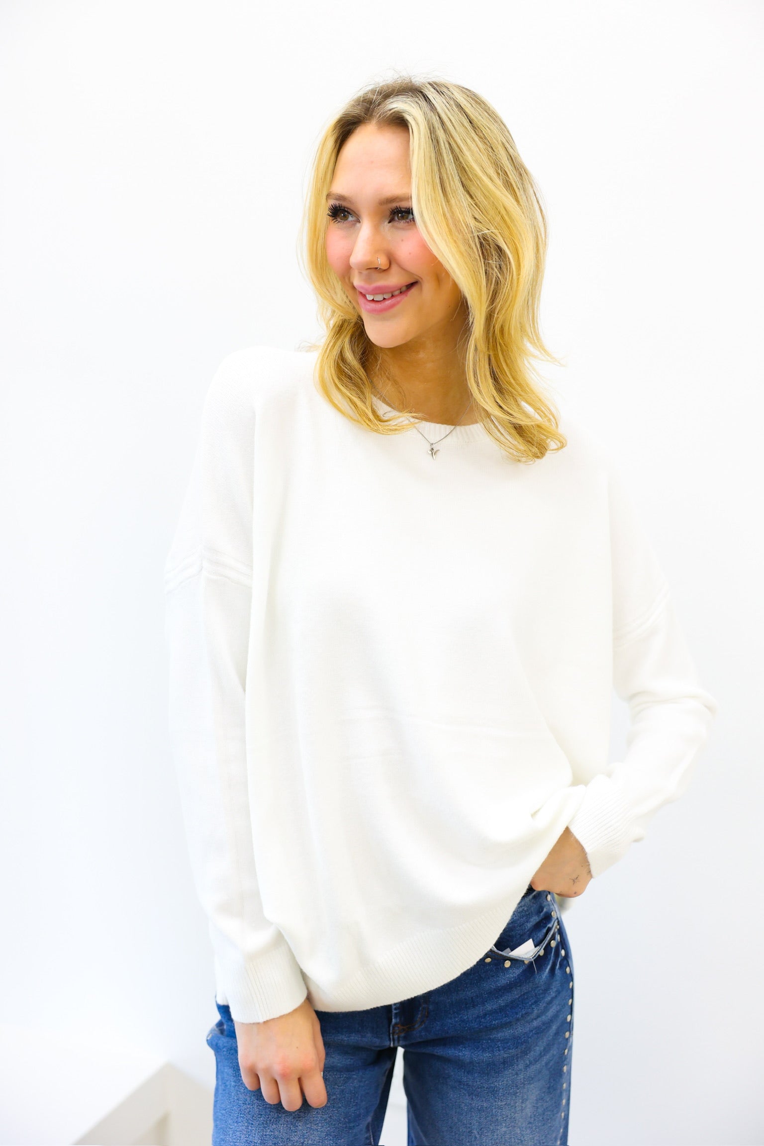 Woman wearing a white sweater and blue jeans against a white background