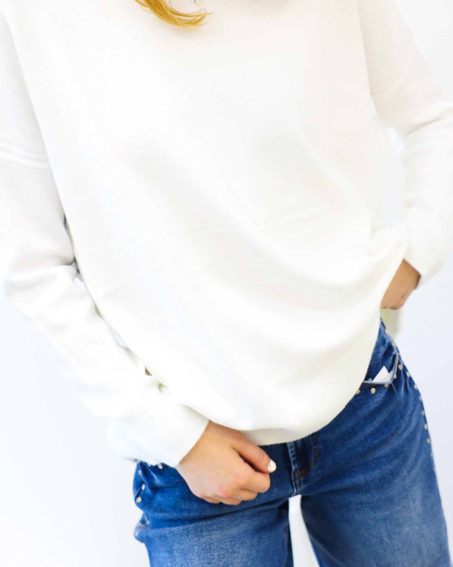 Person wearing a white sweater and blue jeans on a plain background