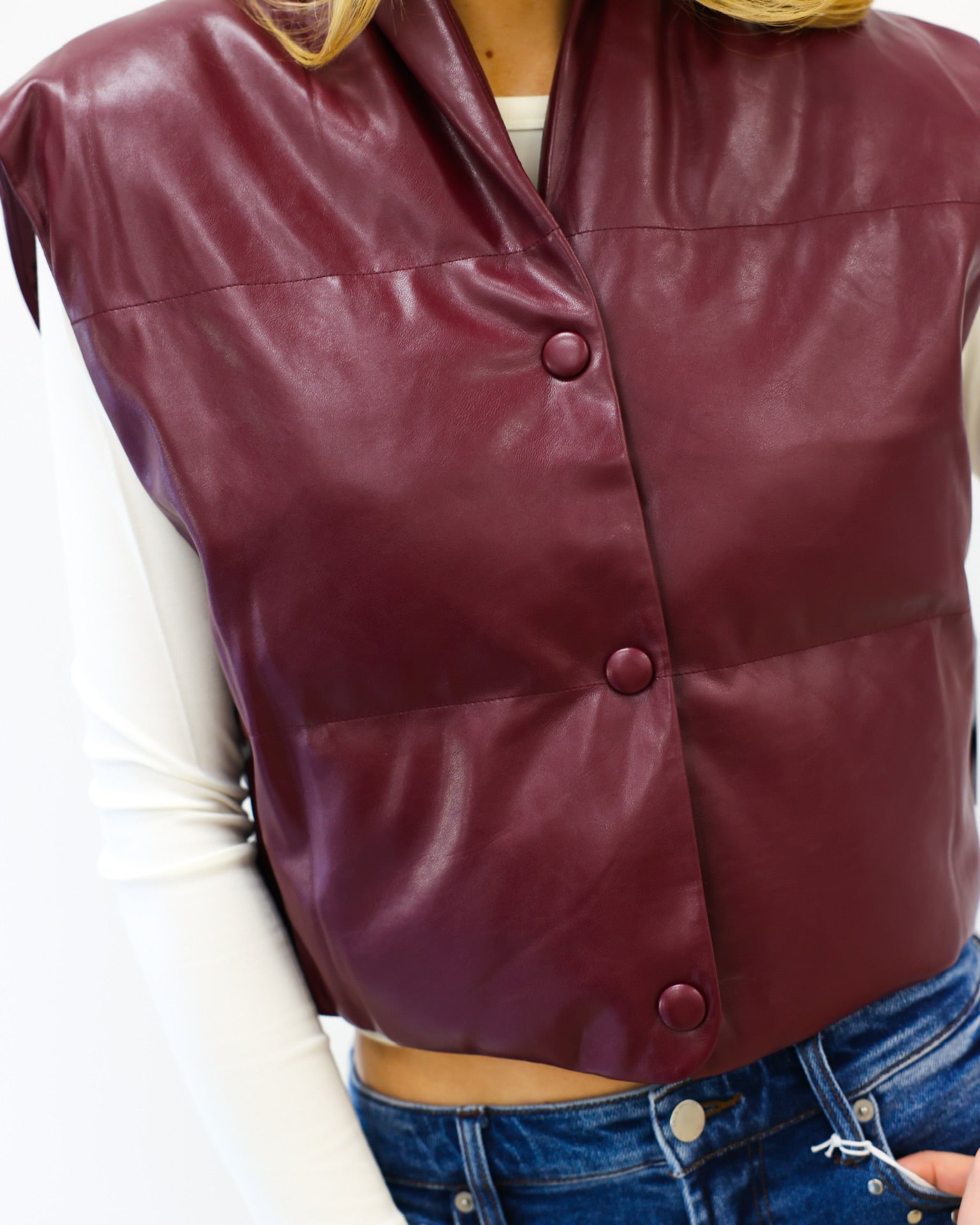 Maroon leather vest worn by a person with a white shirt and blue jeans.