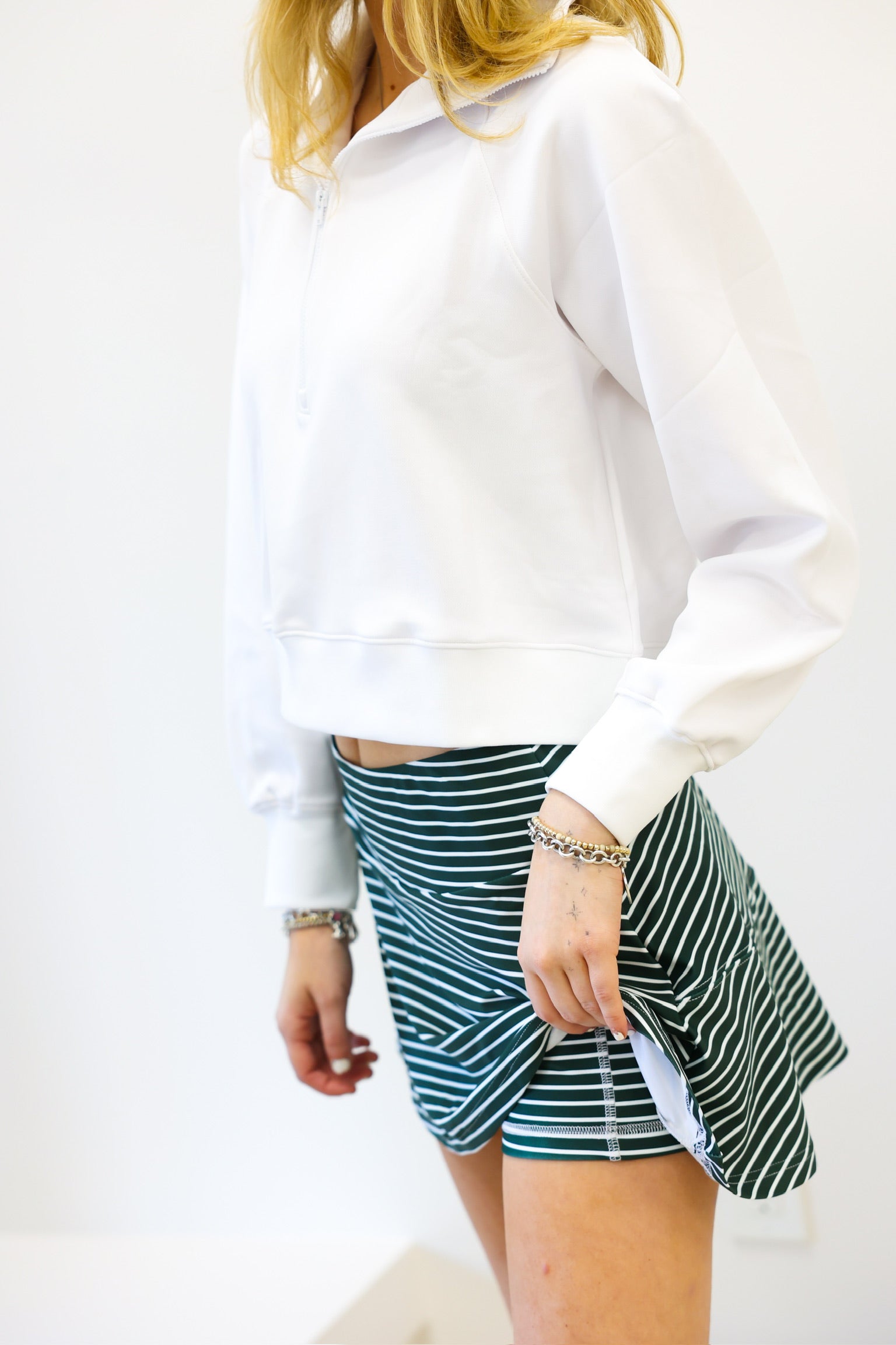 Person wearing a white sweatshirt and green striped shorts on a plain background