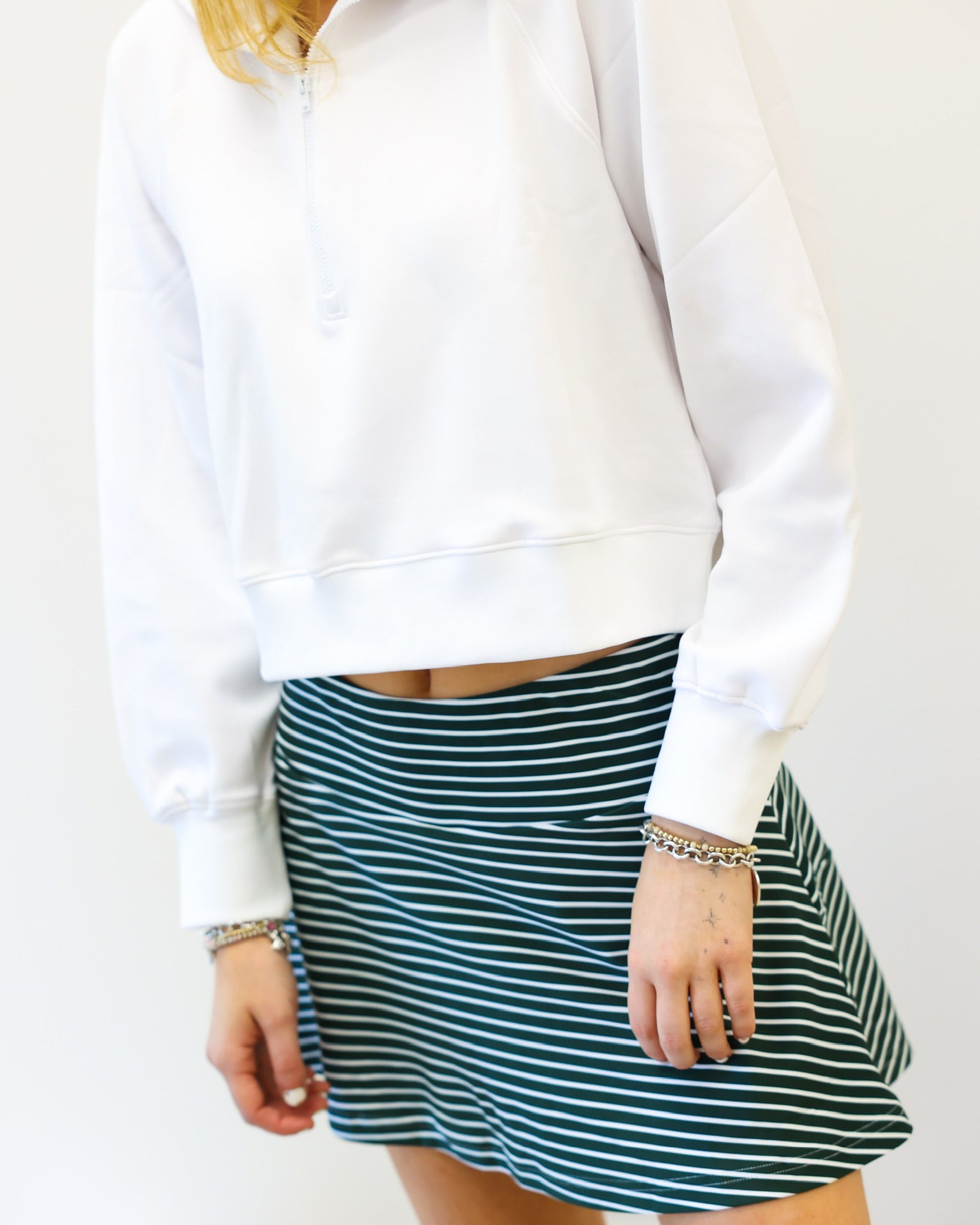 Person wearing a white sweater and green striped skirt on a plain background