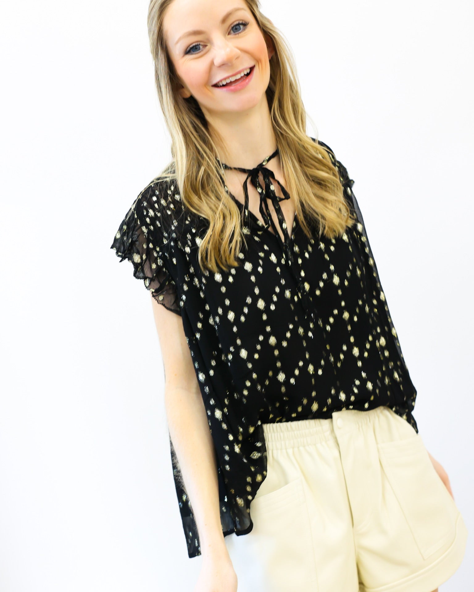 Woman wearing a black top with white patterns and beige shorts on a white background