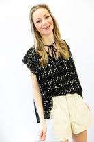 Woman wearing a black top with white patterns and beige shorts on a white background