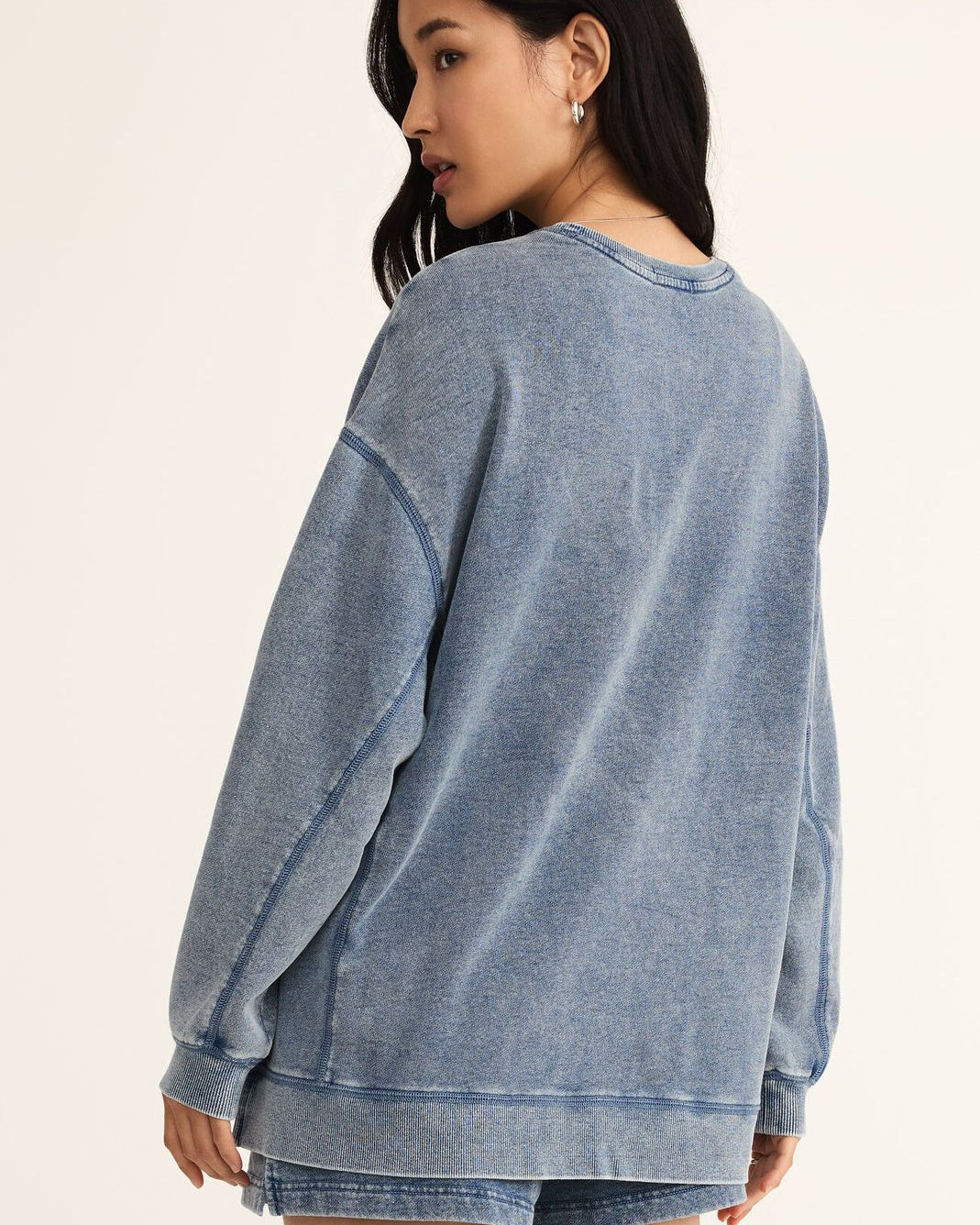 Woman wearing a blue sweatshirt and denim shorts on a beige background