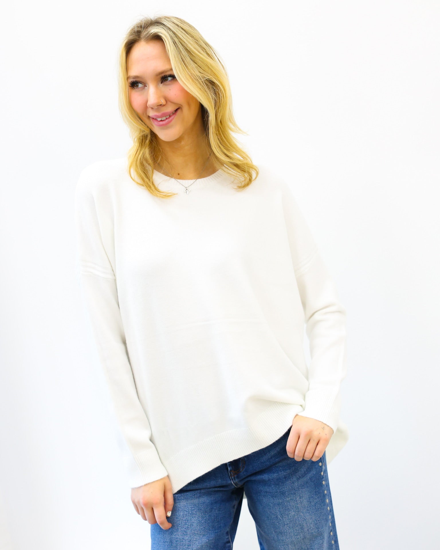 Woman wearing a white sweater and blue jeans on a white background