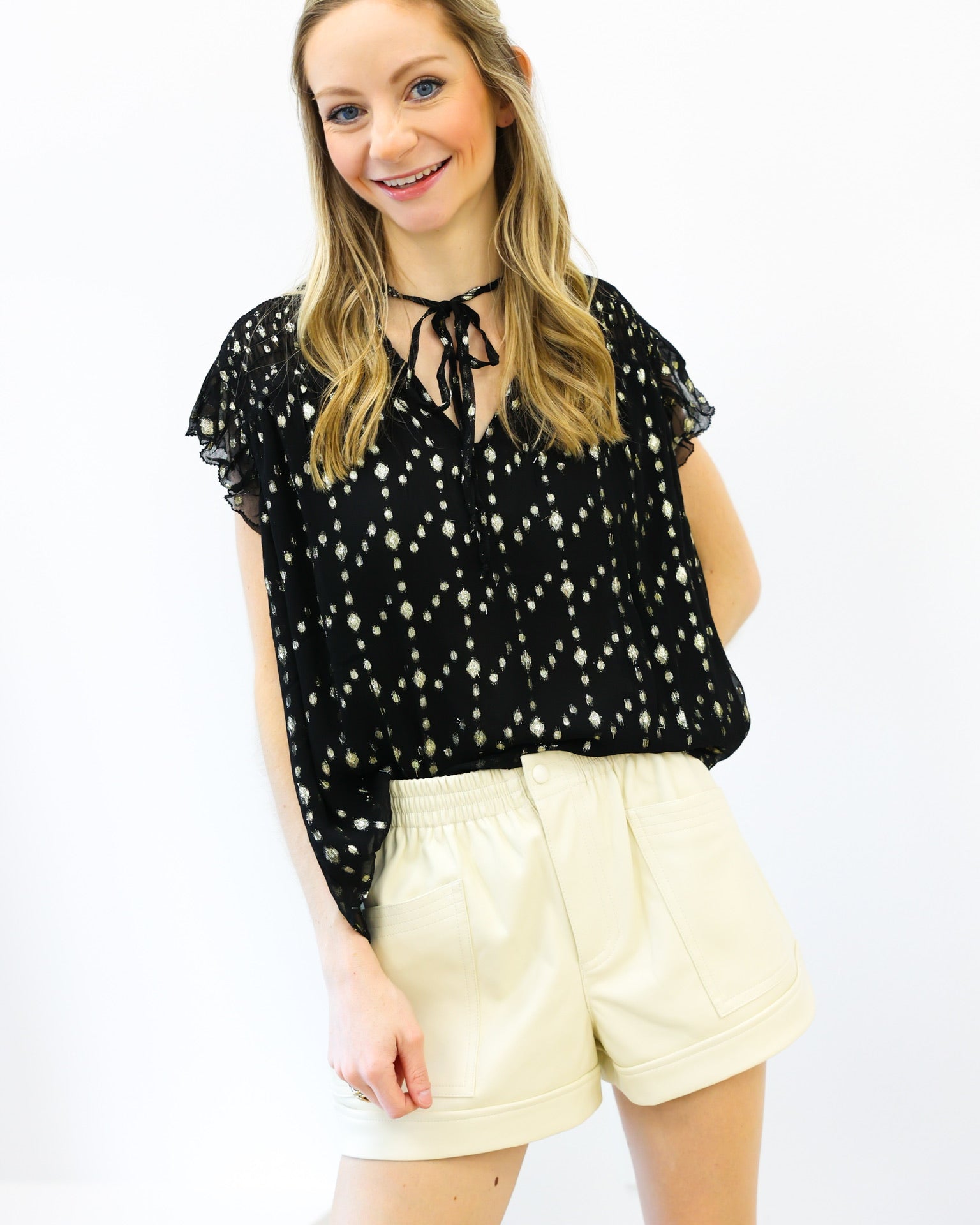 Woman wearing a black blouse with white polka dots and beige shorts on a white background