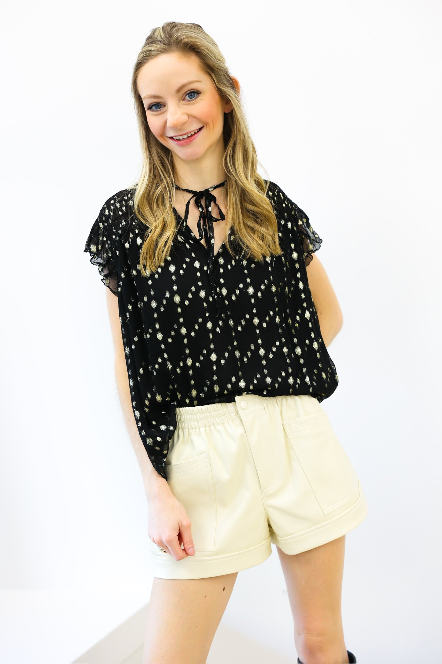 Woman wearing a black blouse with white polka dots and beige shorts on a white background