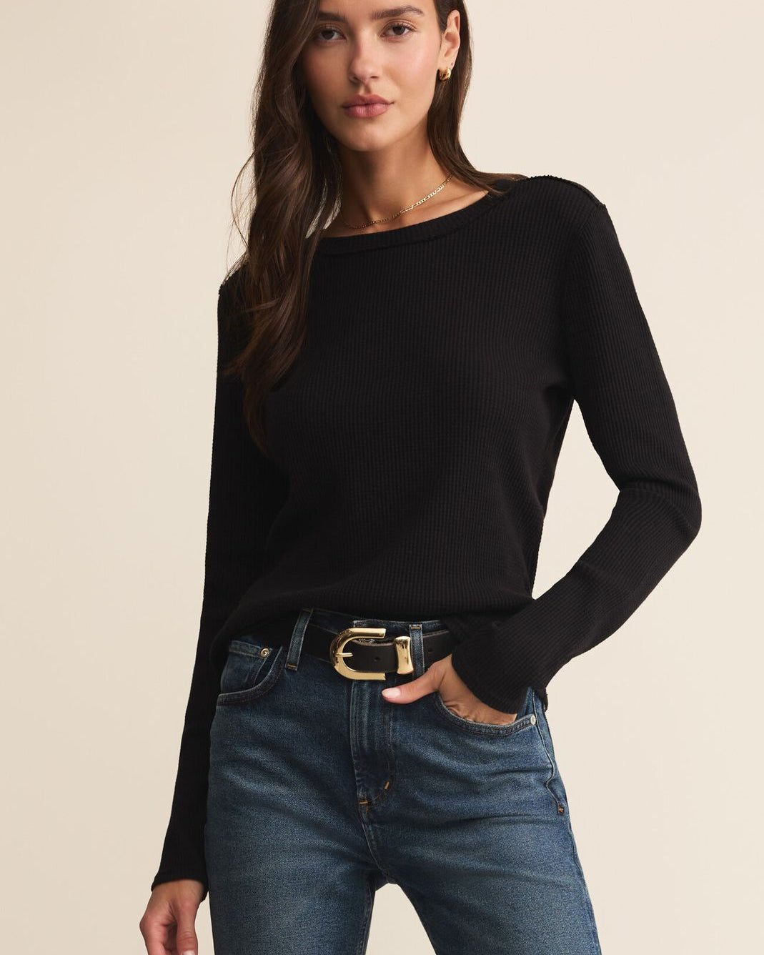 Woman wearing a black sweater and blue jeans on a beige background