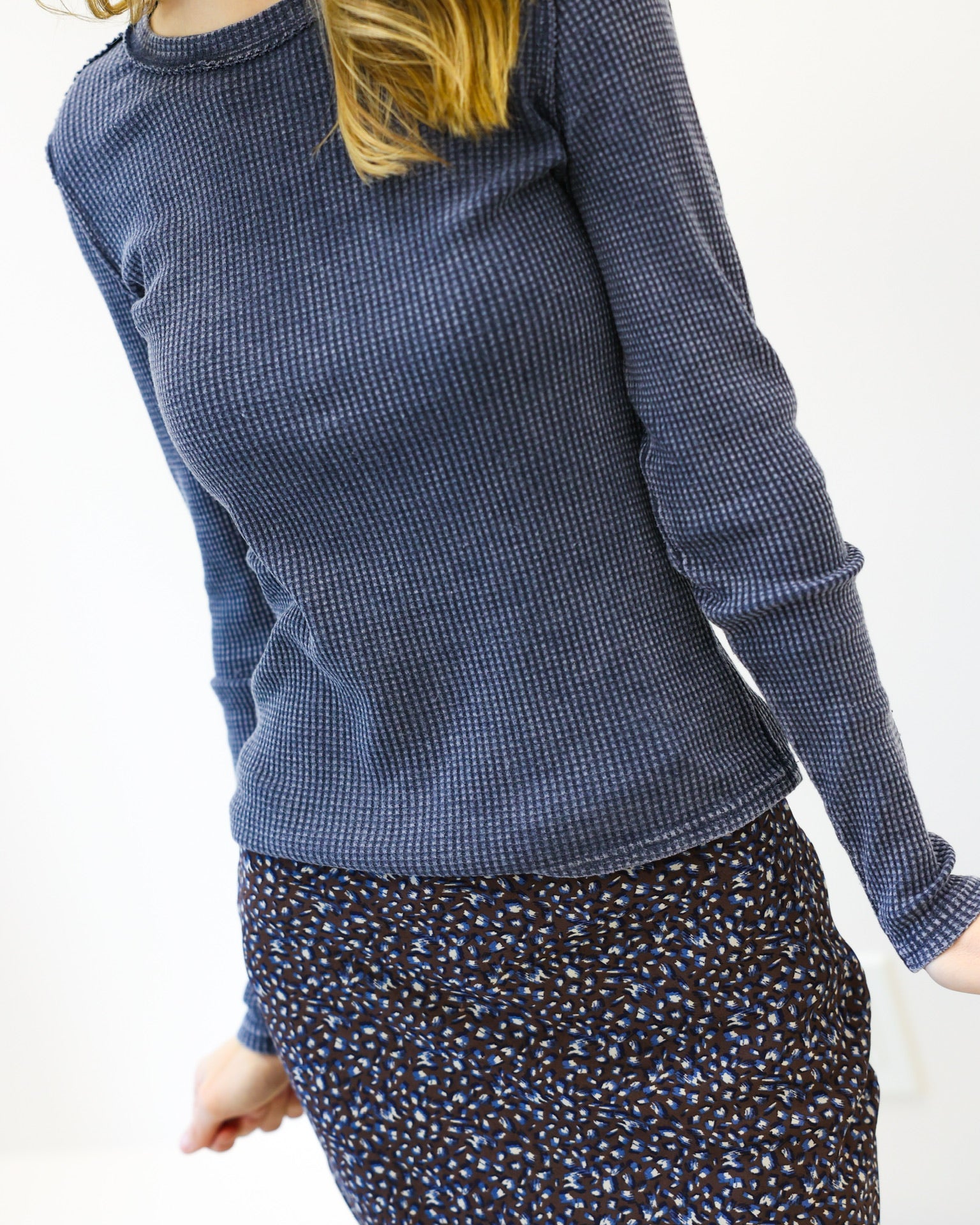 Person wearing a blue textured sweater and patterned skirt on a white background