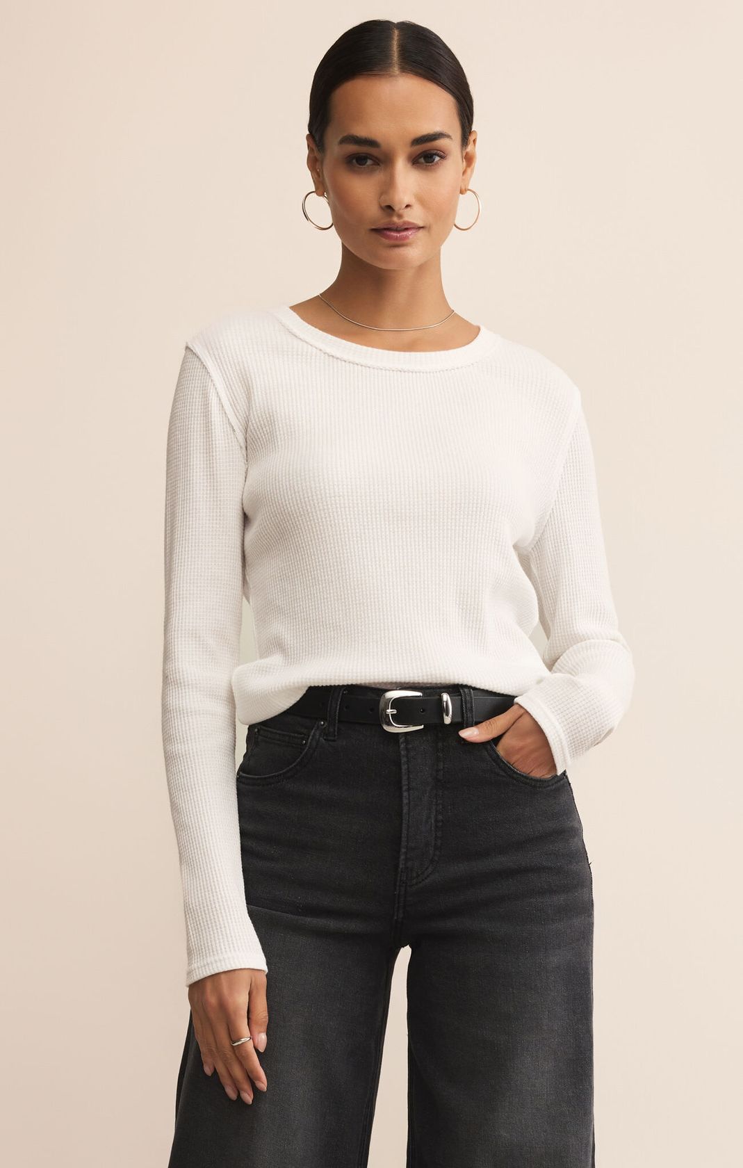 Woman wearing a white sweater and black jeans against a beige background