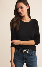 Woman wearing a black sweater and blue jeans on a beige background