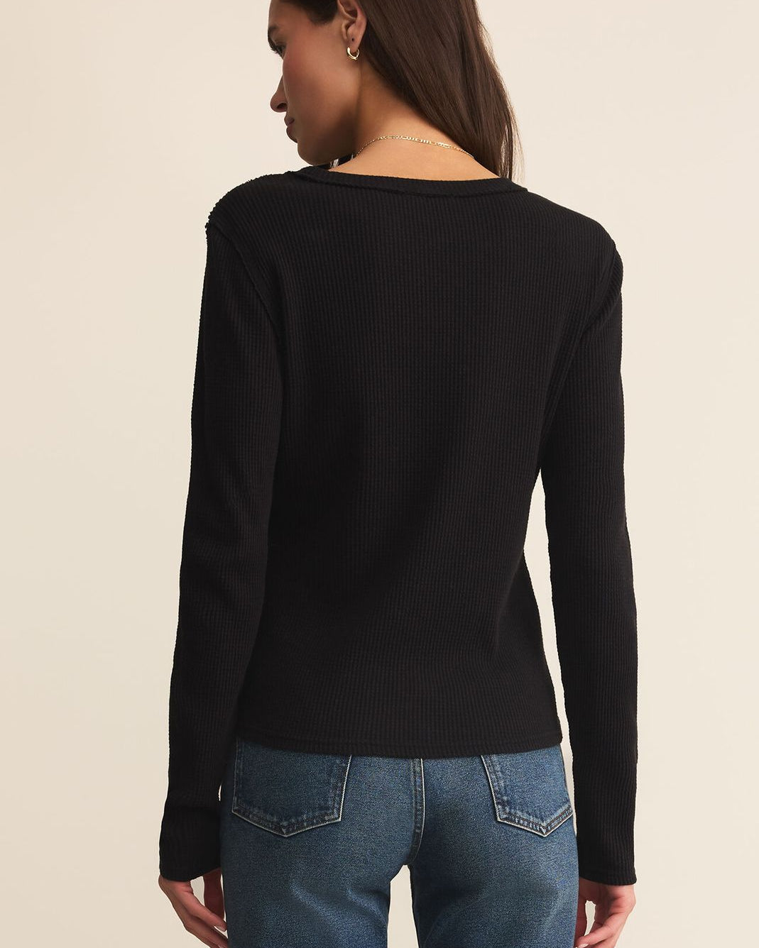 Person wearing a black long-sleeve top and blue jeans on a beige background