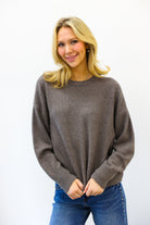 Woman wearing a brown sweater and blue jeans against a white background