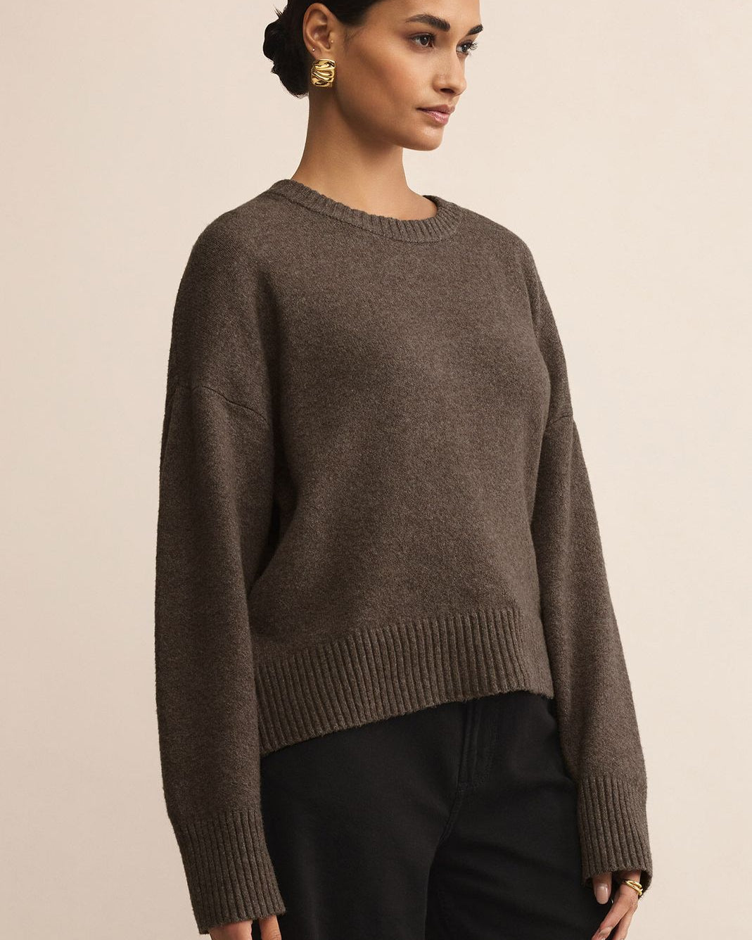 Woman wearing a brown sweater and black pants against a beige background