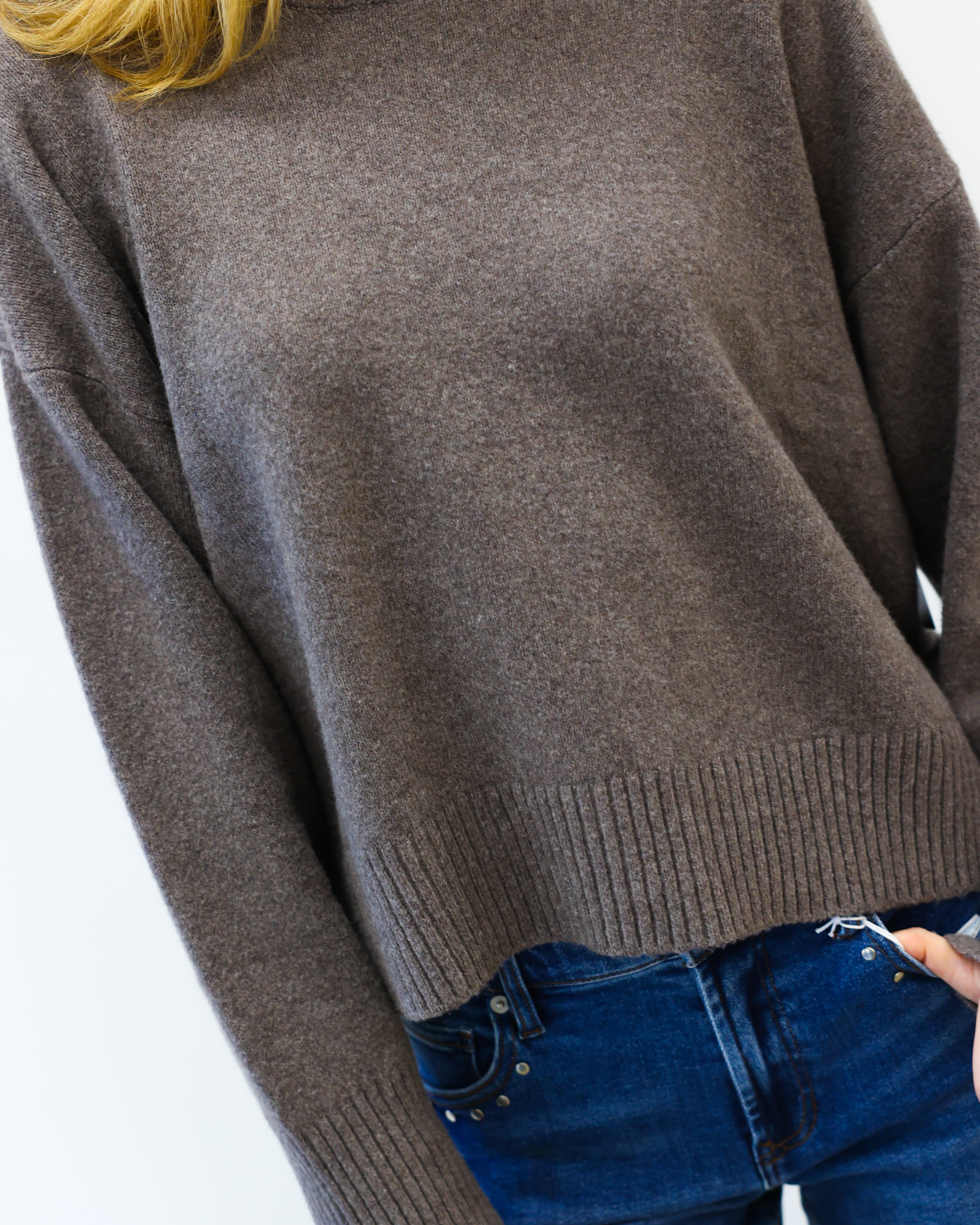 Person wearing a brown sweater and blue jeans on a white background
