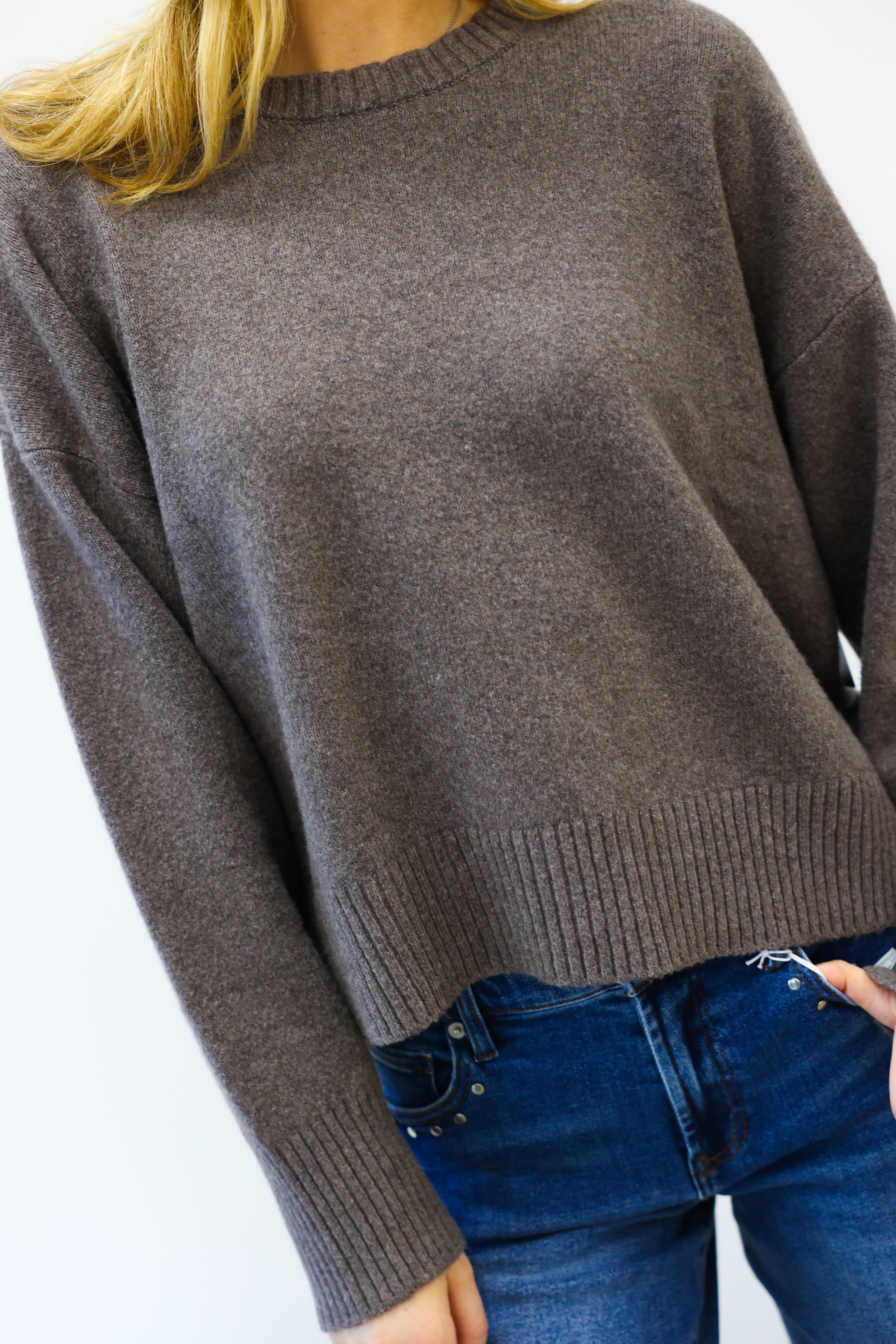 Person wearing a brown sweater and blue jeans on a white background