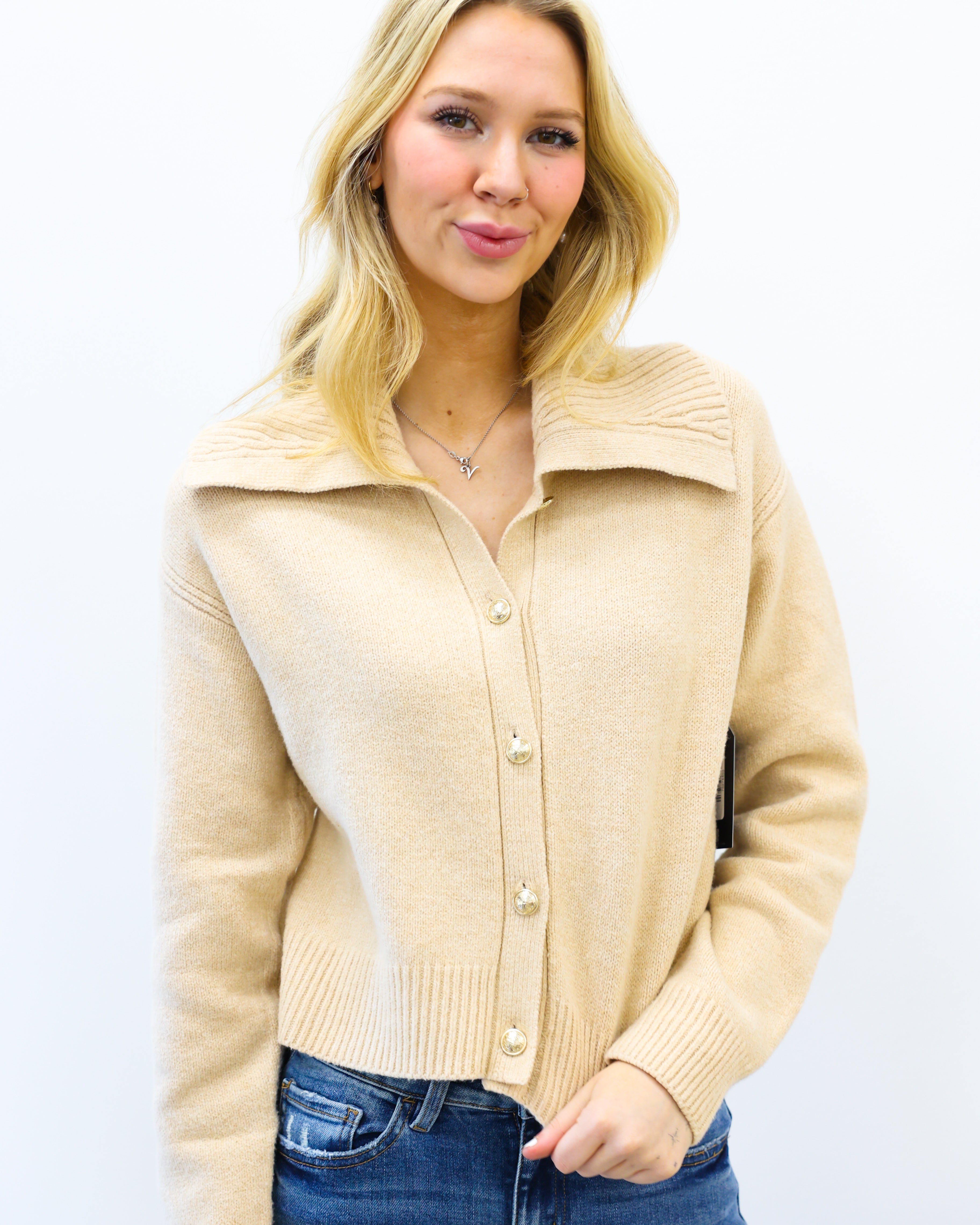 Woman wearing a beige cardigan and blue jeans on a white background