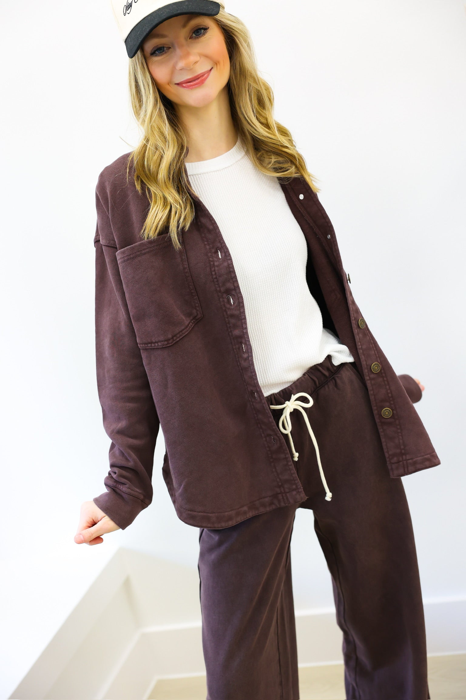 Woman wearing a brown jacket and pants with a white shirt, standing against a plain background.