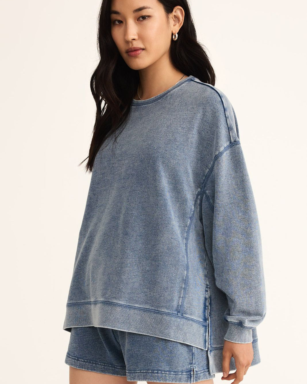 Woman wearing a blue denim sweatshirt and shorts on a beige background
