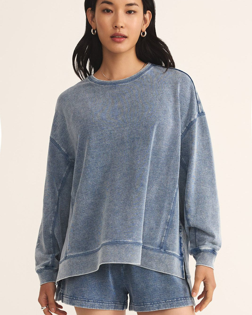 Woman wearing a blue sweatshirt and shorts on a beige background