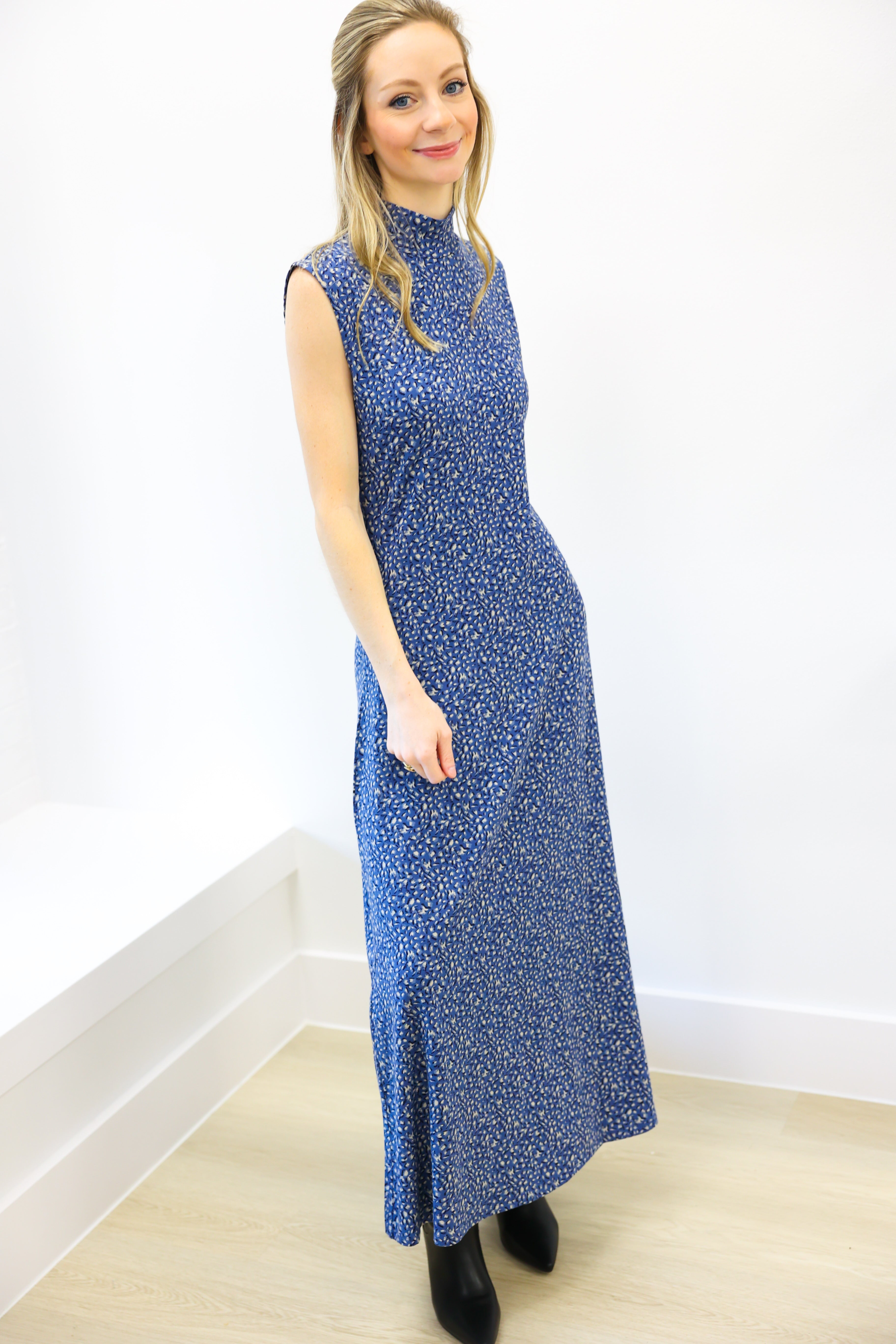 Woman wearing a blue patterned dress against a white wall.