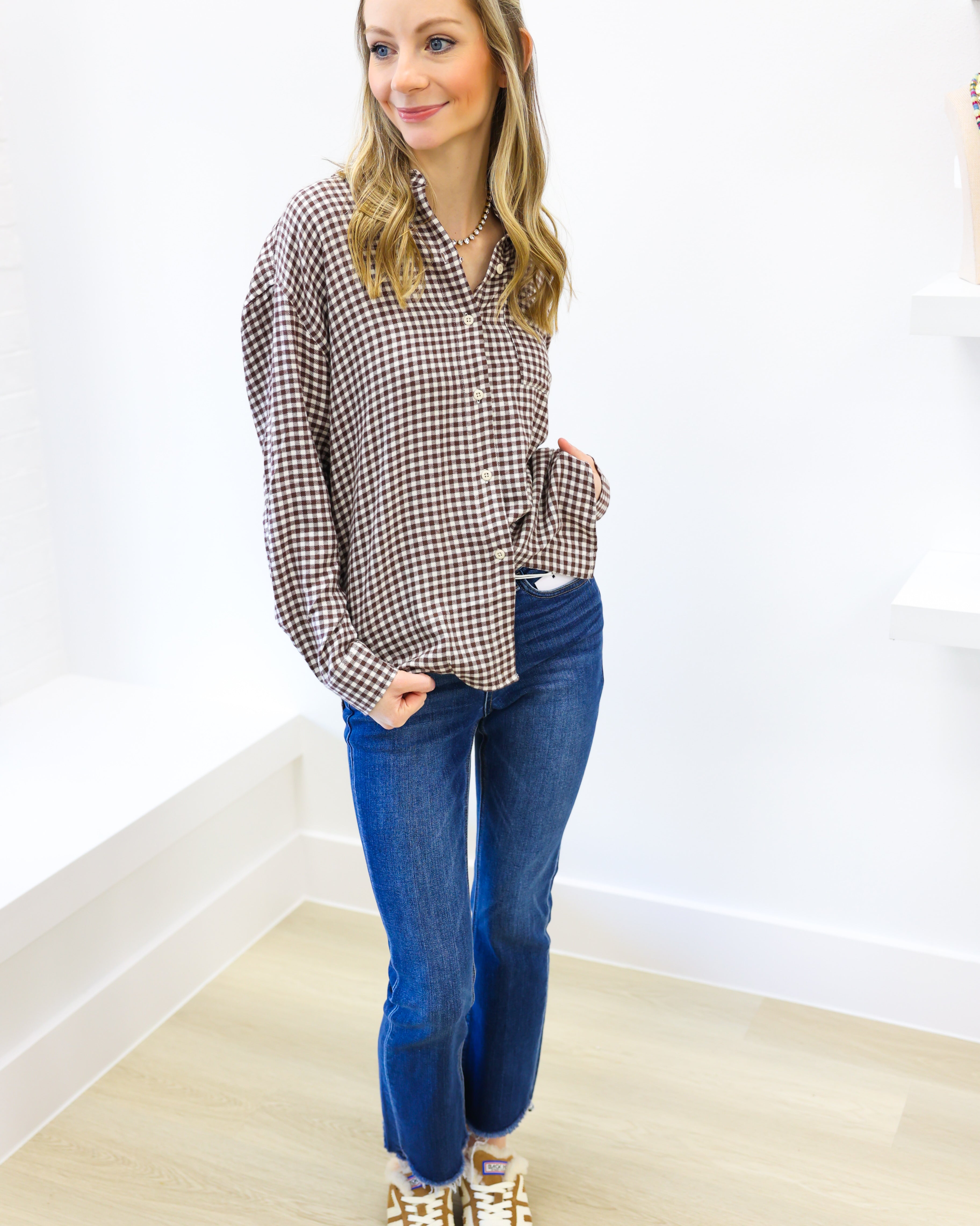 Woman wearing a plaid shirt and blue jeans against a white wall.