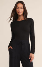 Woman wearing a black long-sleeve top and pants on a beige background