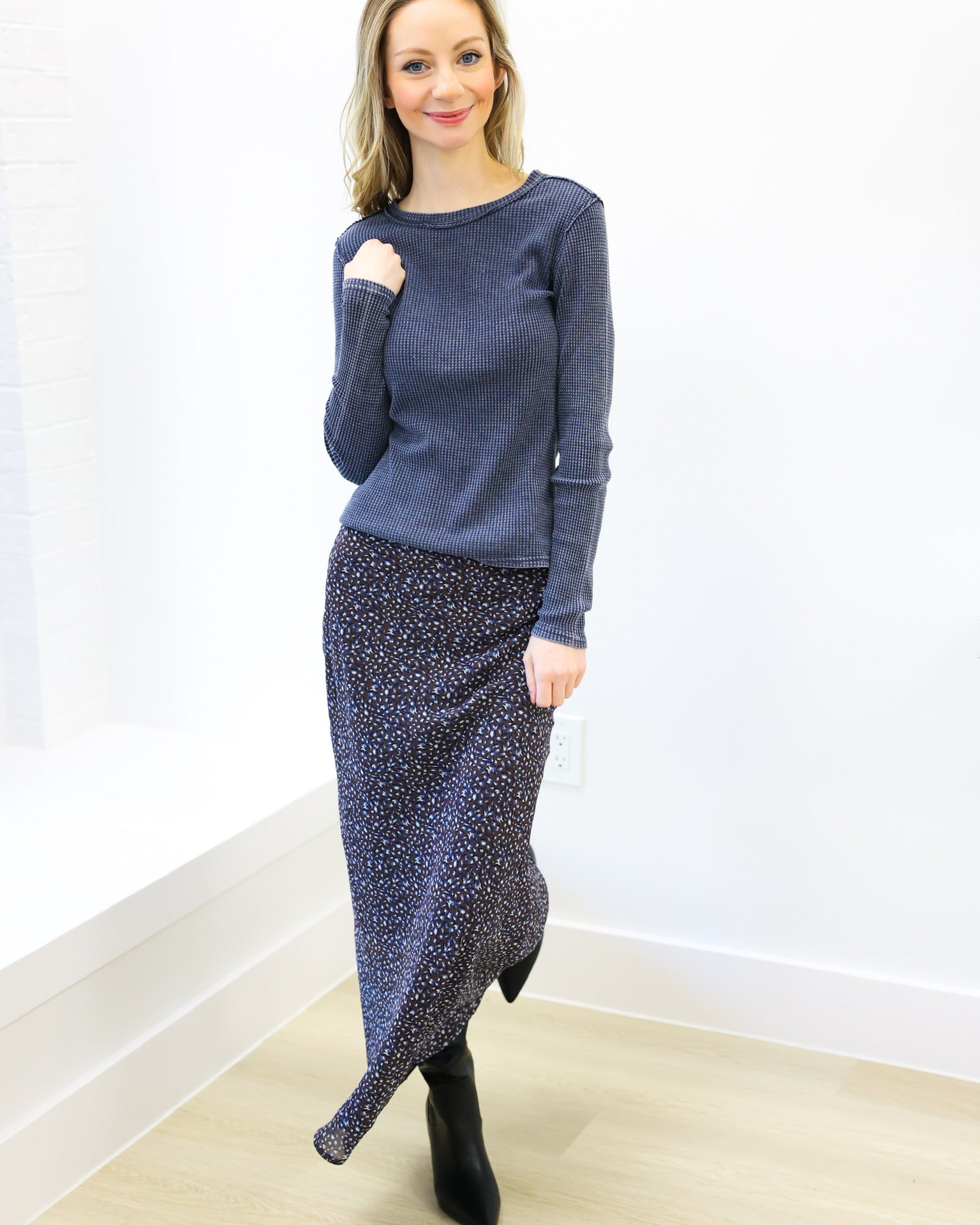 Woman wearing a blue sweater and patterned skirt against a white wall.