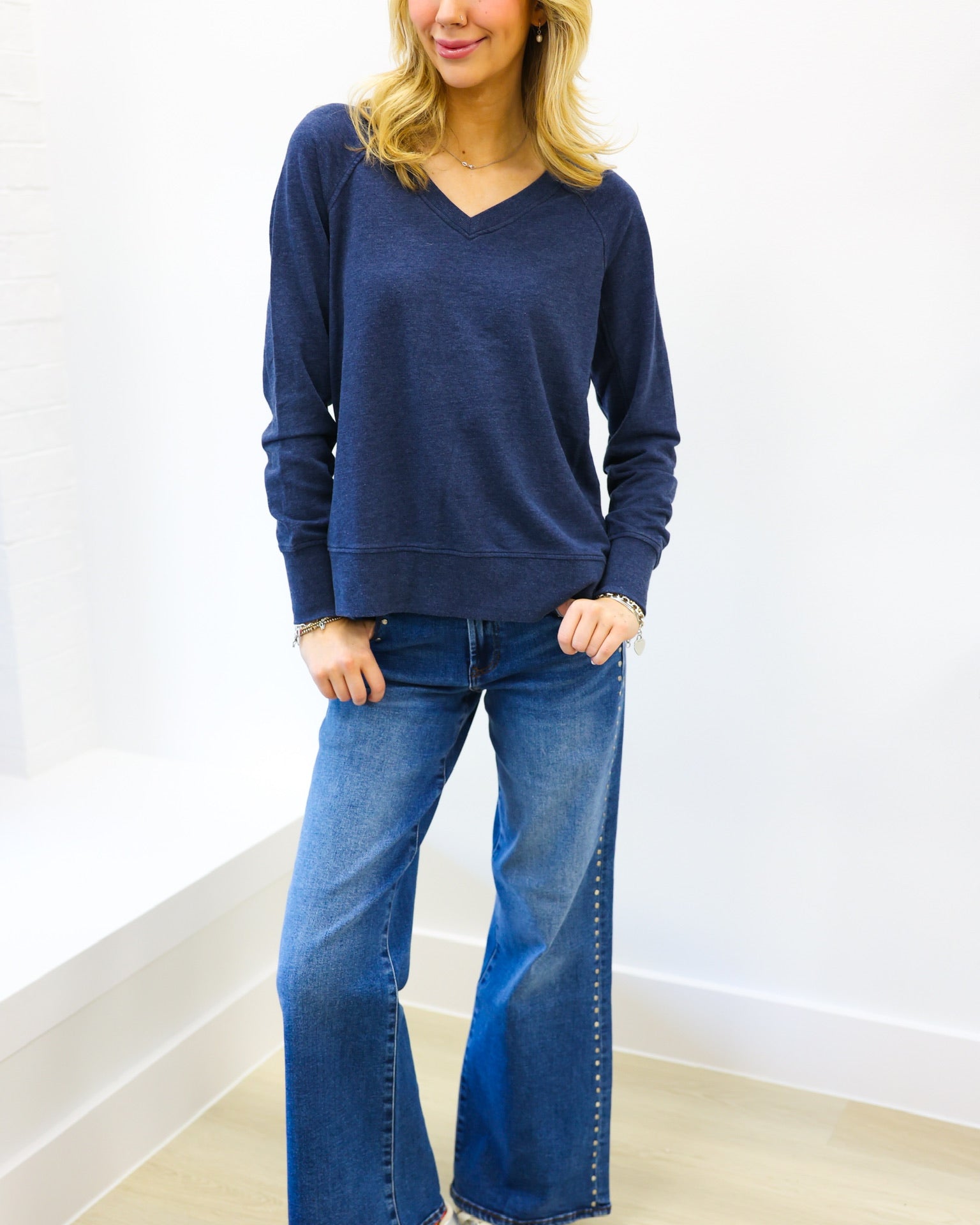 Woman wearing a blue sweater and blue jeans against a white wall.