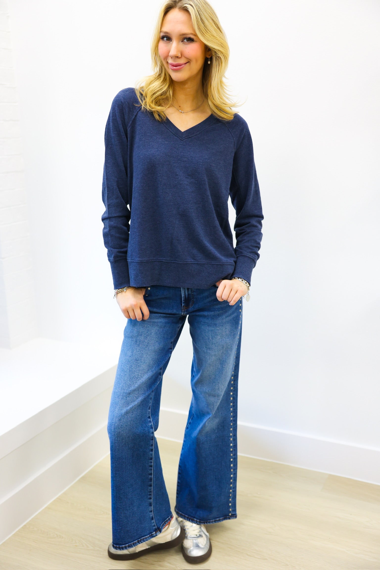 Woman wearing a blue sweater and blue jeans against a white wall.