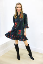 Woman wearing a dark floral dress with bell sleeves and black knee-high boots against a white background
