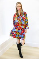 Woman wearing a colorful floral dress with black knee-high boots against a white wall.