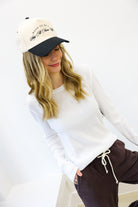 Woman wearing a white long-sleeve shirt, brown pants, and a cap with text on a white background