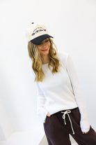 Woman wearing a white sweatshirt and dark pants with a cap on a white background