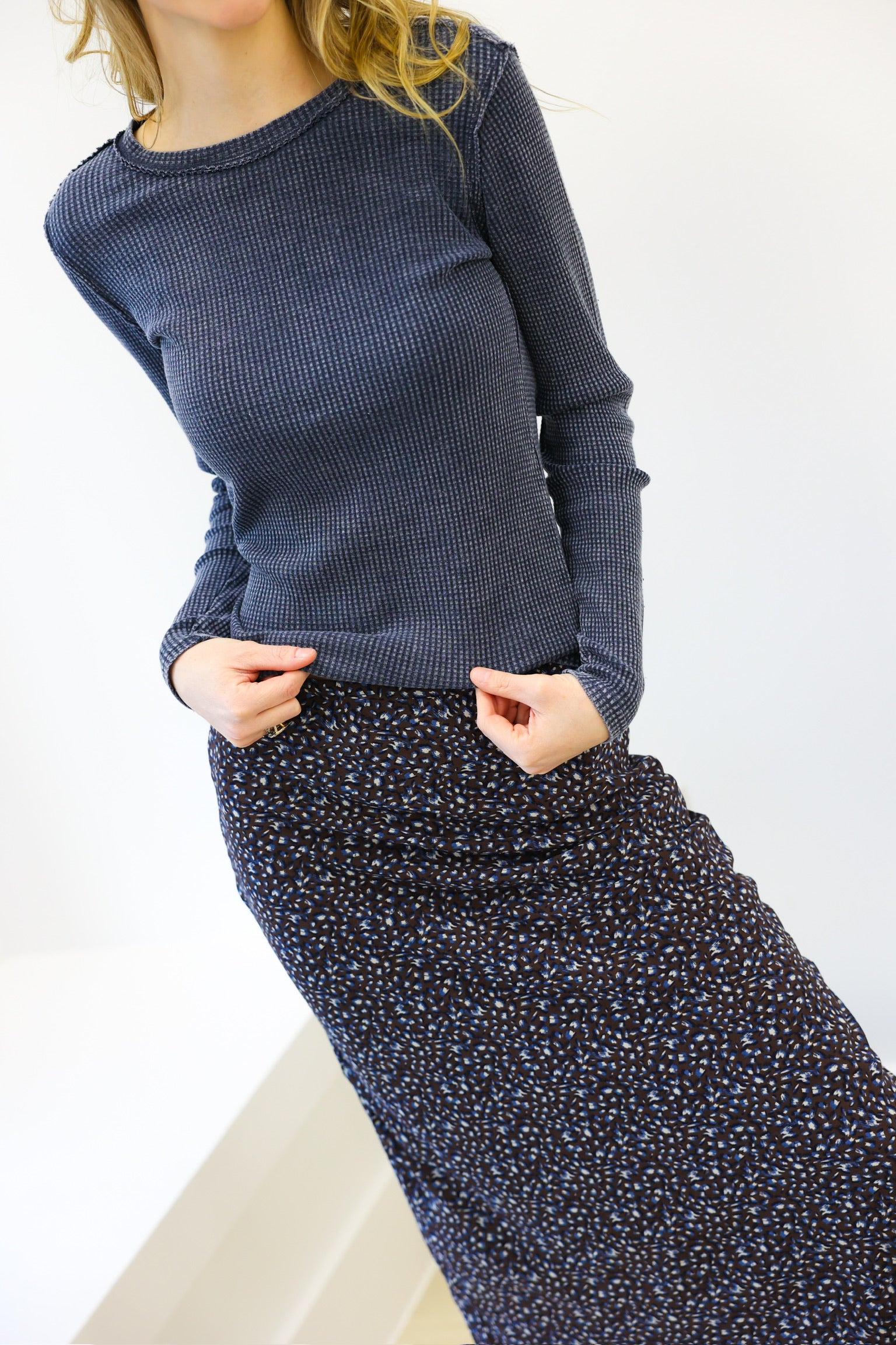 Woman wearing a blue textured sweater and patterned skirt against a white background