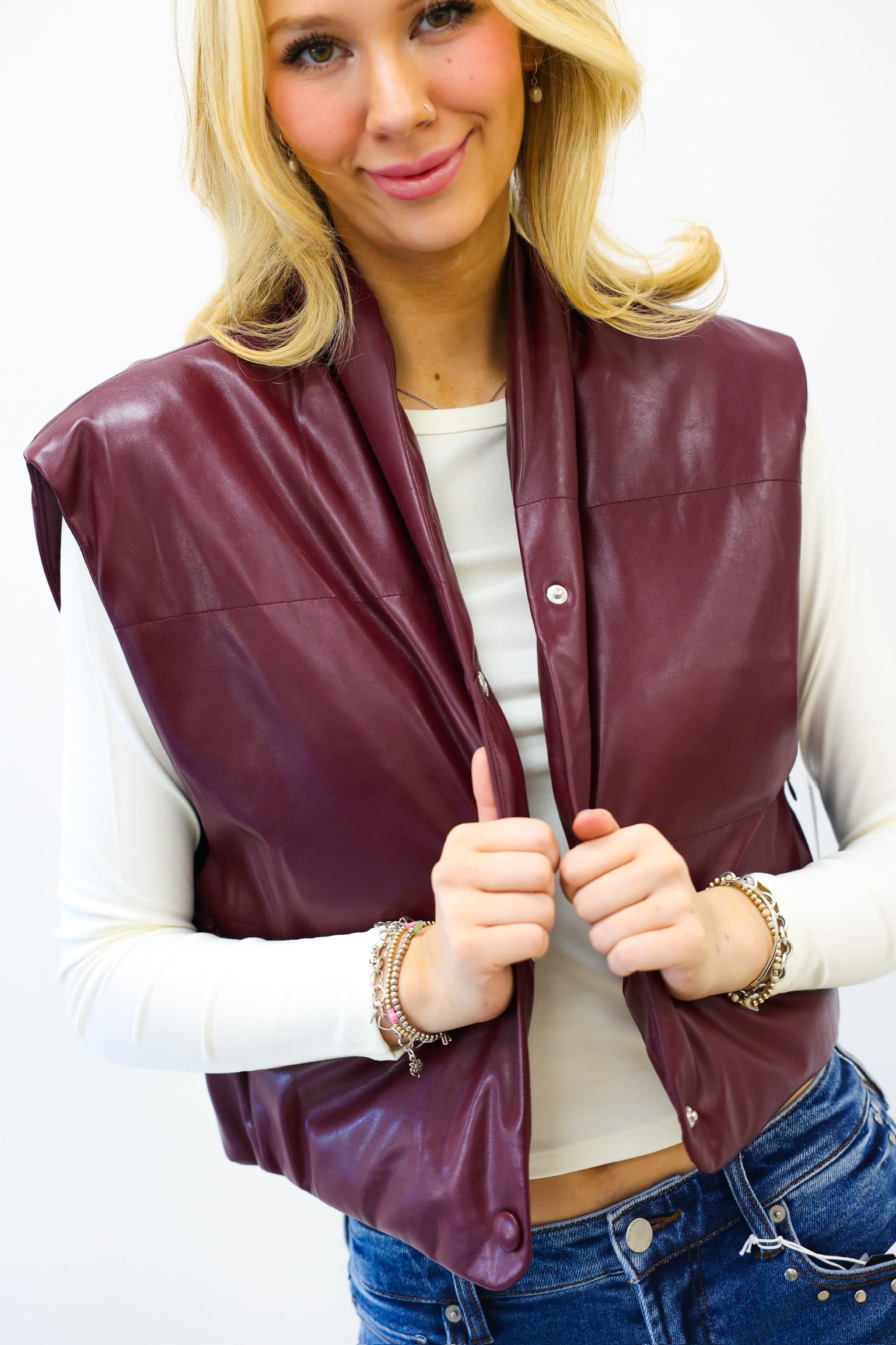 Woman wearing a maroon leather vest over a white shirt with blue jeans on a white background