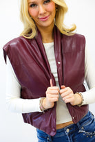 Woman wearing a maroon leather vest over a white shirt with blue jeans on a white background