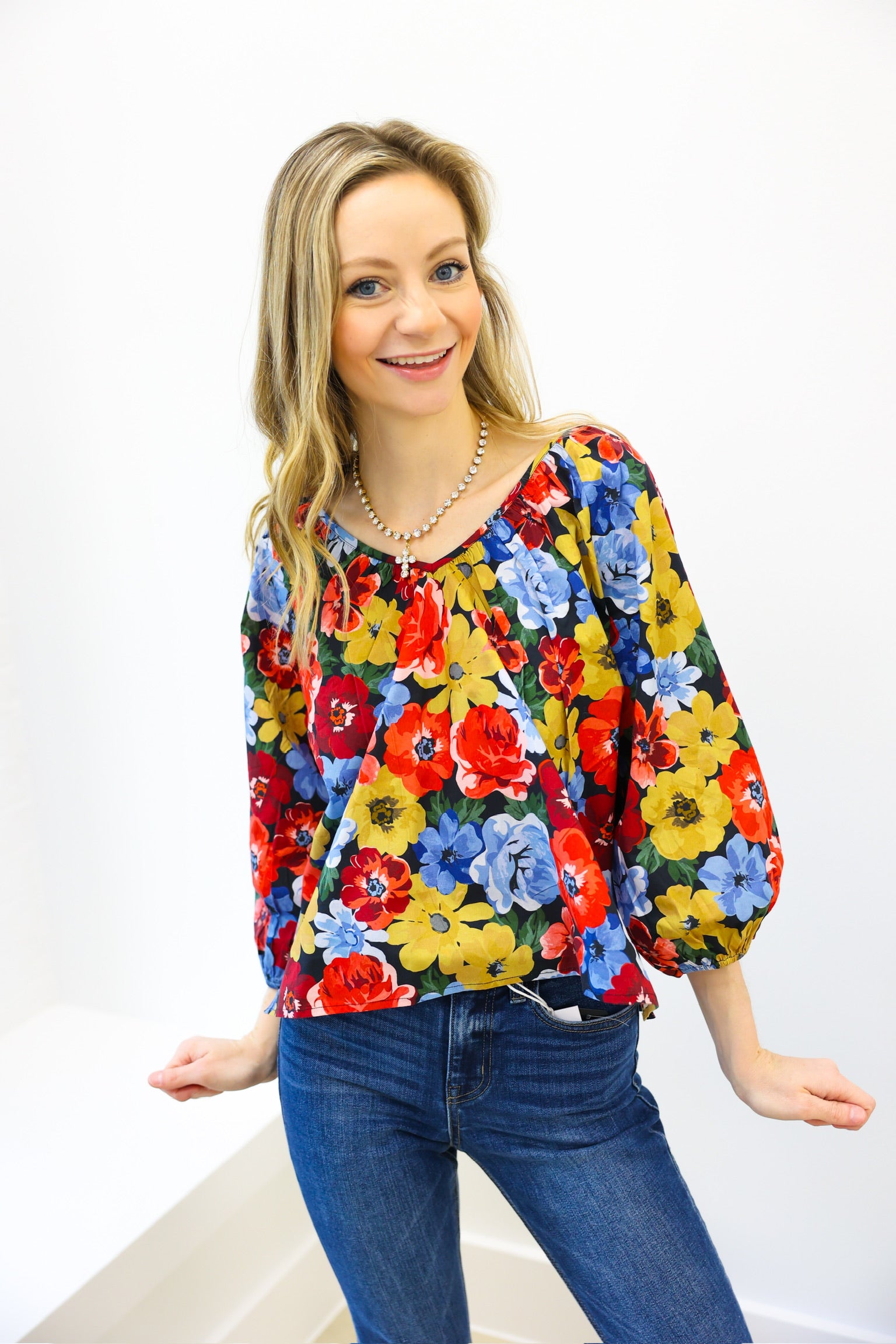 Woman wearing a colorful floral blouse and blue jeans on a white background