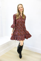 Woman wearing a red floral dress with bell sleeves and black boots in a minimal indoor setting.