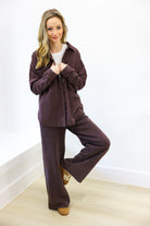 Woman wearing a brown tracksuit standing against a white wall.