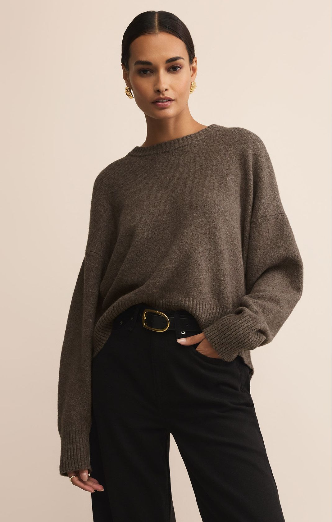 Woman wearing a brown sweater and black pants against a beige background