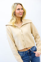 Woman wearing a beige cardigan and blue jeans against a white background