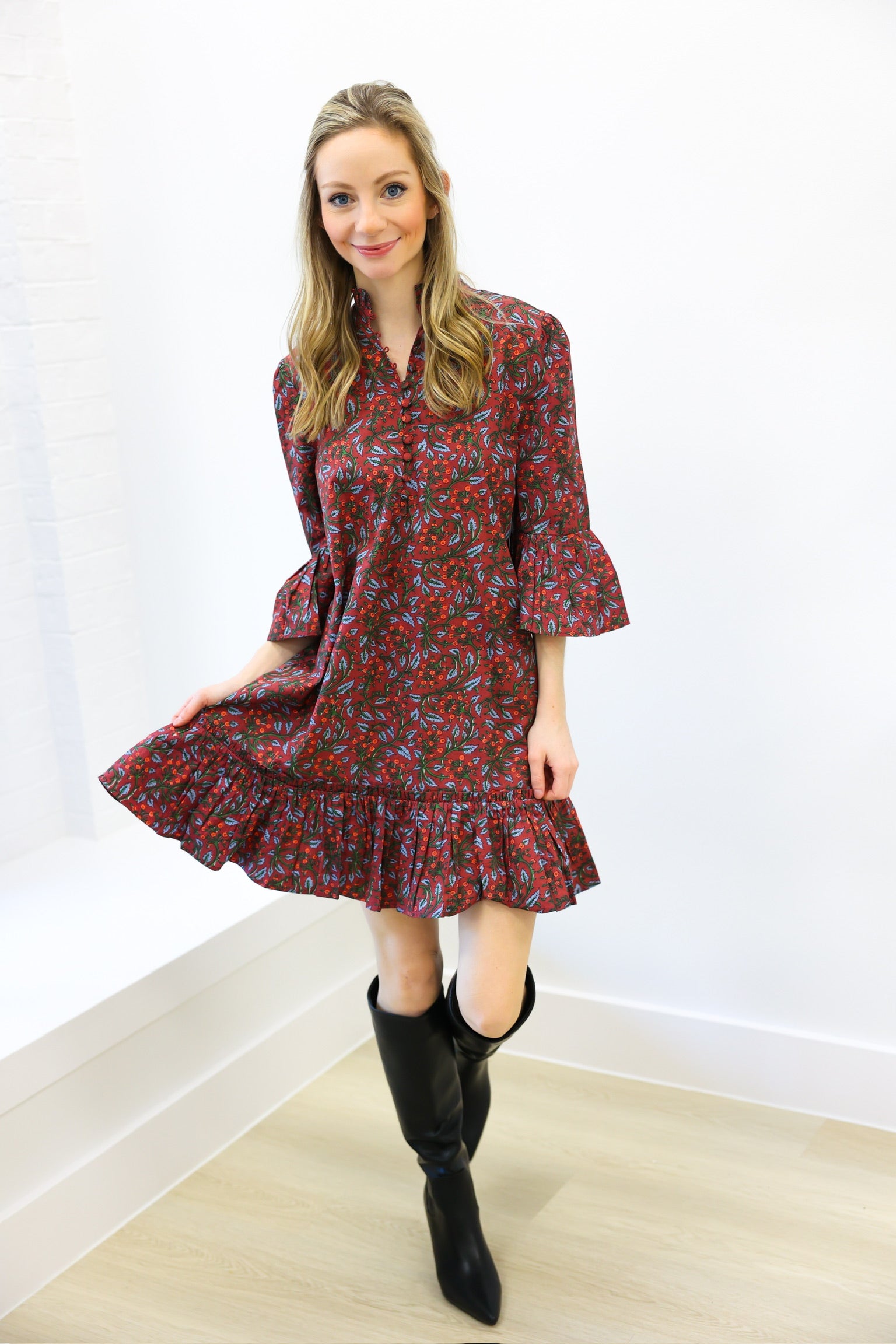 Woman wearing a red floral dress and black knee-high boots against a white background
