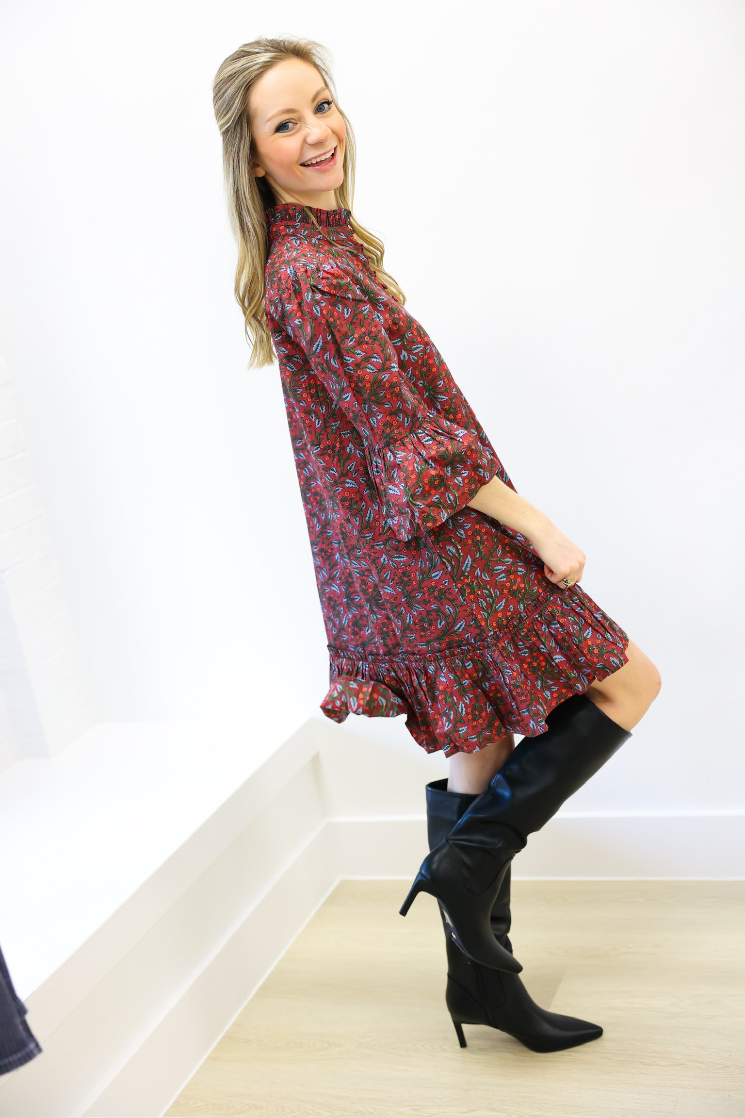 Woman wearing a red floral dress and black knee-high boots on a white background