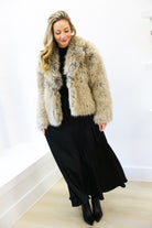 Woman wearing a fur coat over a black dress against a white wall.