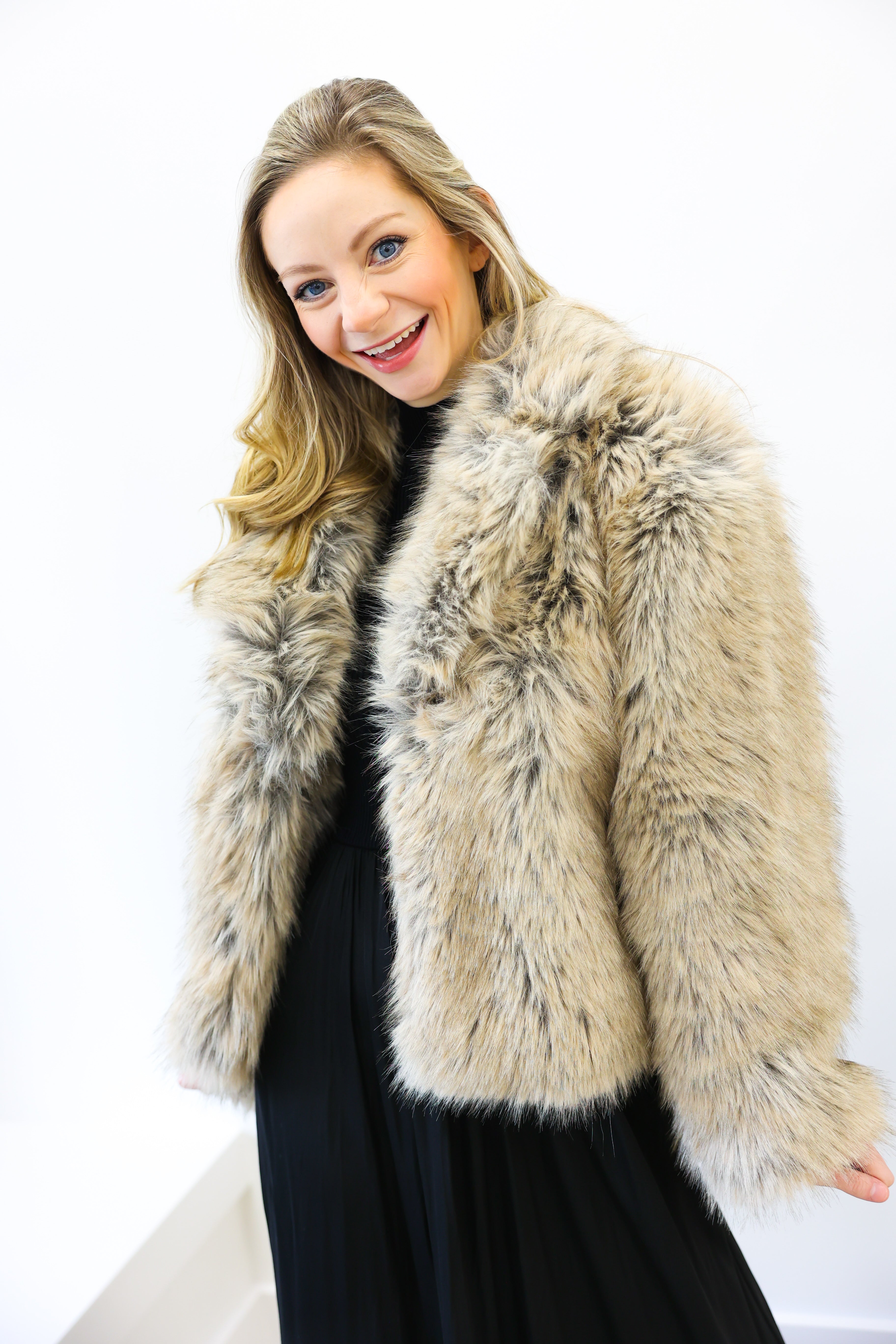 Woman wearing a beige fur coat against a white background